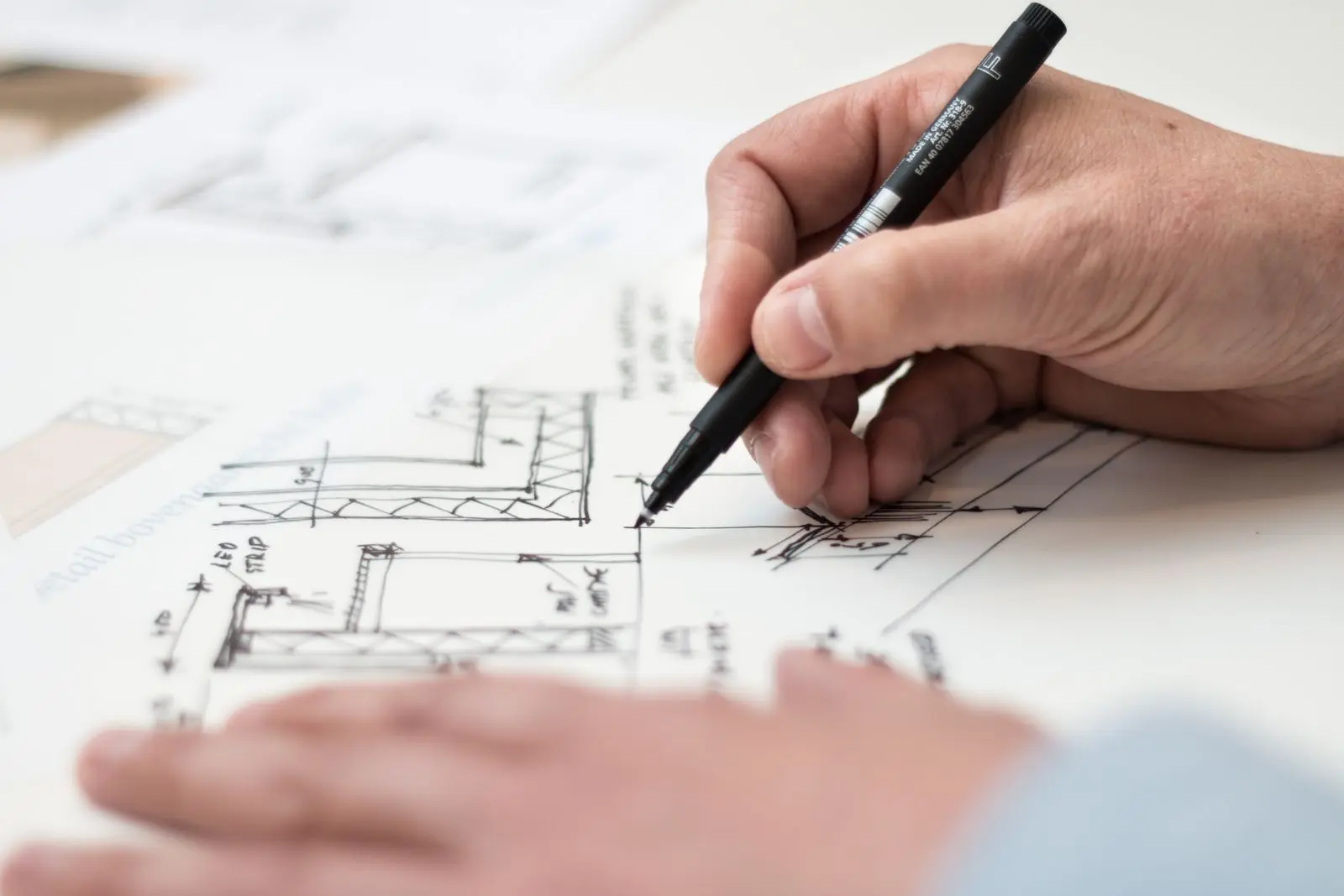 Architect's hand drafting a detailed floor plan with a pen