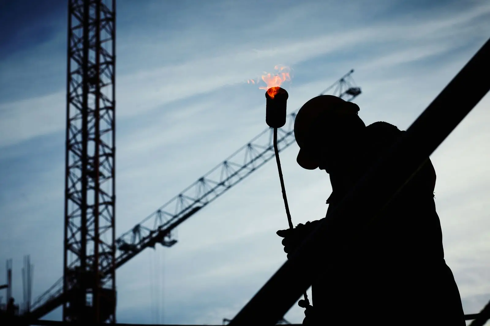 Silhouette of a welder working at height with a crane in the background